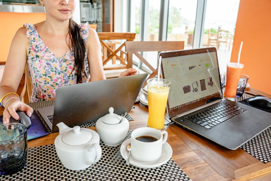 Une femme boit dans une tasse à café et tape sur le clavier d'un ordinateur portable, assise sur le canapé de son salon à la maison.